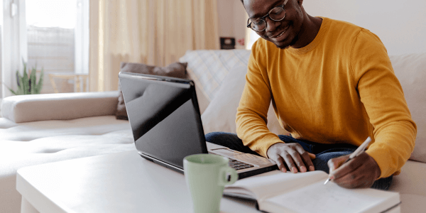 Man writing down notes while working on his laptop